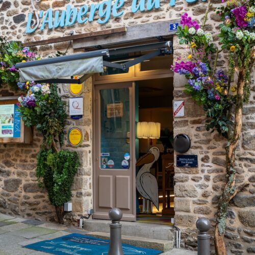 Façade accueillante avec logo bleu turquoise et mur en pierres à L'Auberge du Pélican à Dinan.