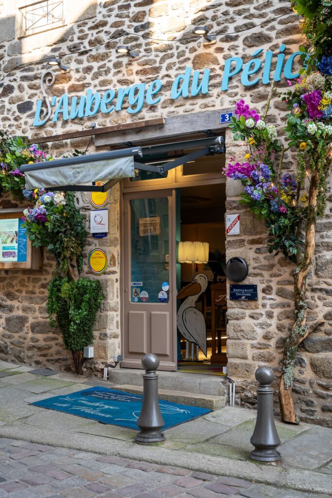 Façade accueillante avec logo bleu turquoise et mur en pierres à L'Auberge du Pélican à Dinan.