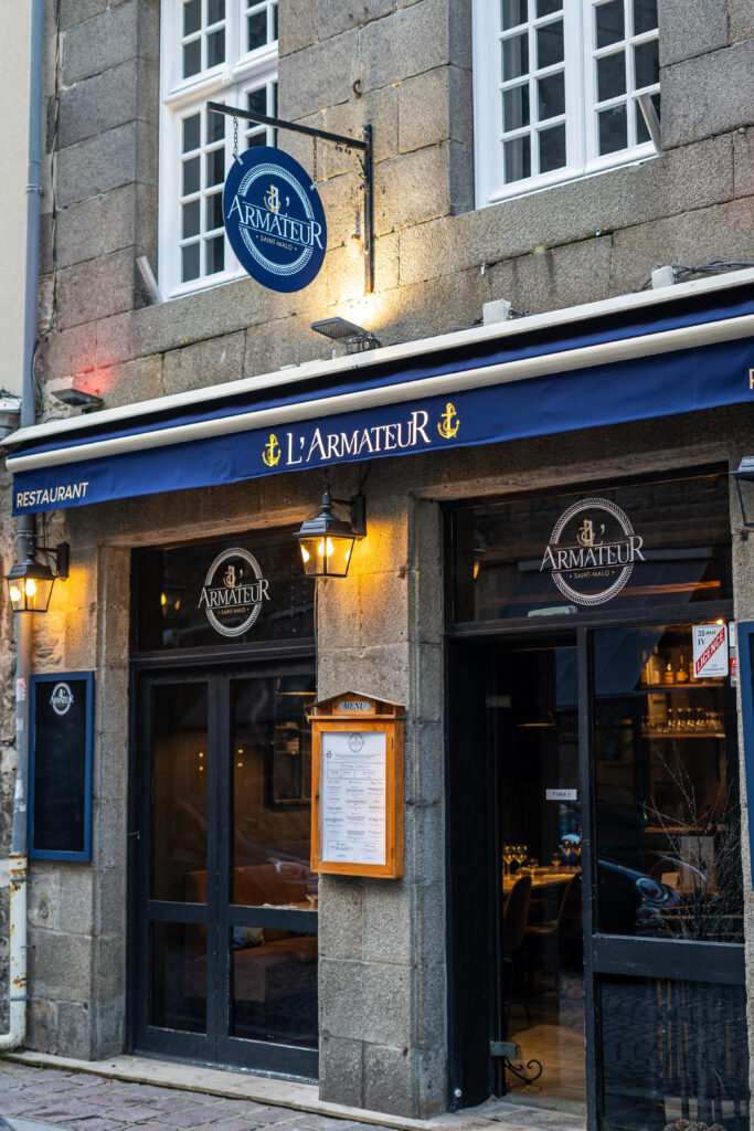 Façade en pierre avec logo bleu du restaurant L'Amateur à Saint-Malo.