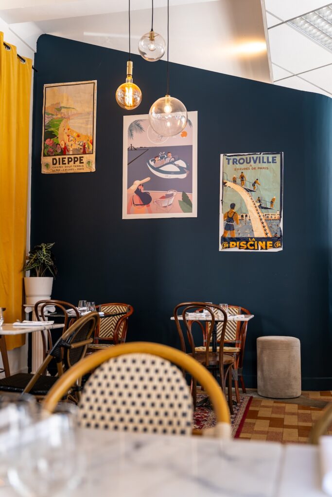 Salle intérieure avec chaises en bois, murs bleu foncé et cadres colorés au Riva Café à Saint-Malo.