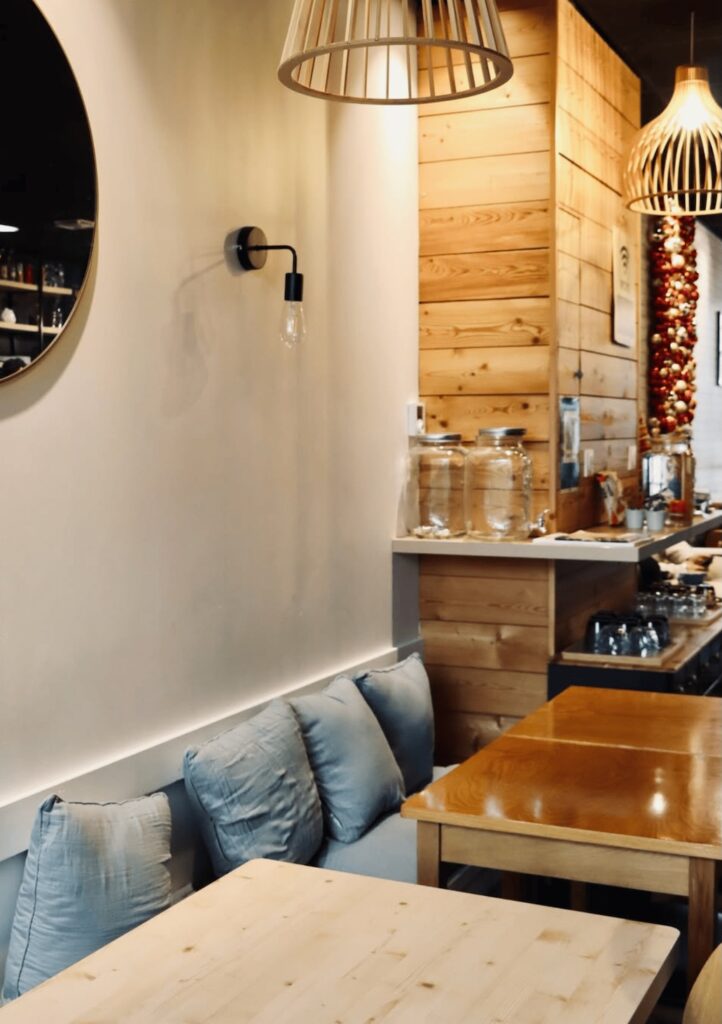 Salle intérieure cosy en bois avec coussins et lumière murale chez Miggy’s Coffee à Saint-Malo.