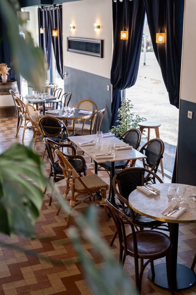 Salle intérieur avec tables dressées et rideaux au Riva Café à Saint-Malo.