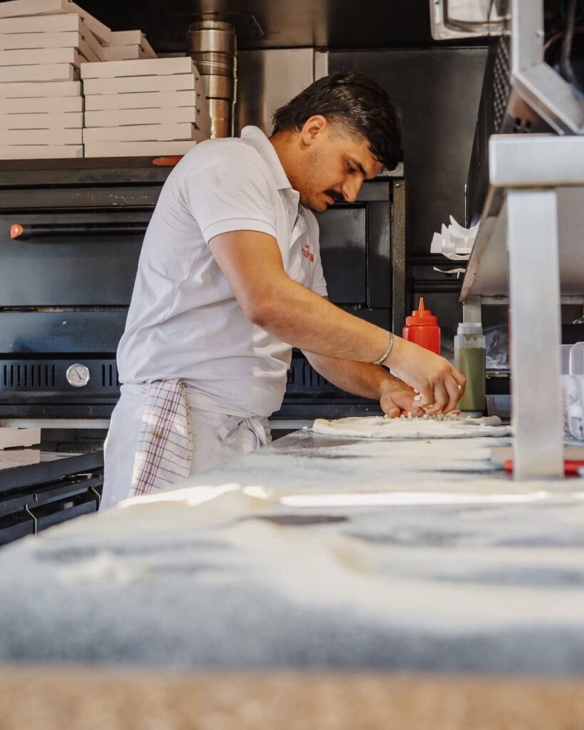 Chef qui met des ingrédients frais sur une pizza maison d'un foodtruck de type cuisine italienne à Billère, près de Pau