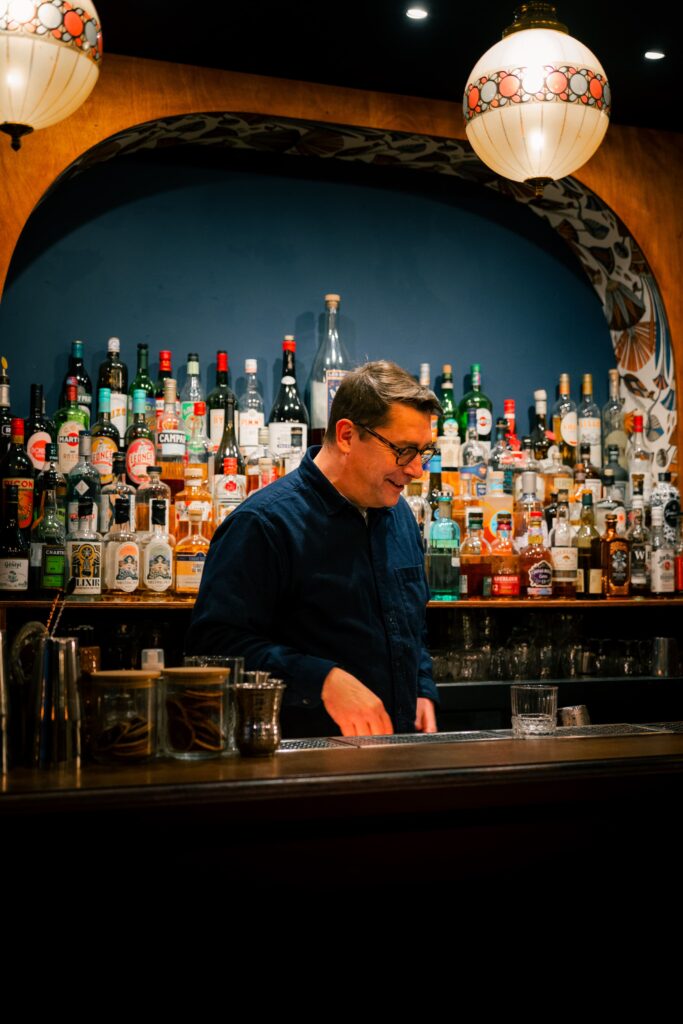 Le barman de Chez René, à Rennes, devant le bar garni.