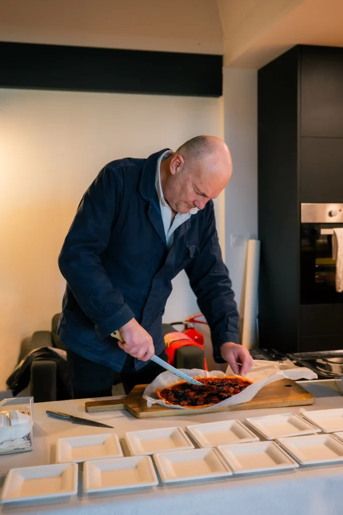 Christophe Boisselier en cuisine, qui est en train de couper une tarte avant de la servir dans les assiettes.